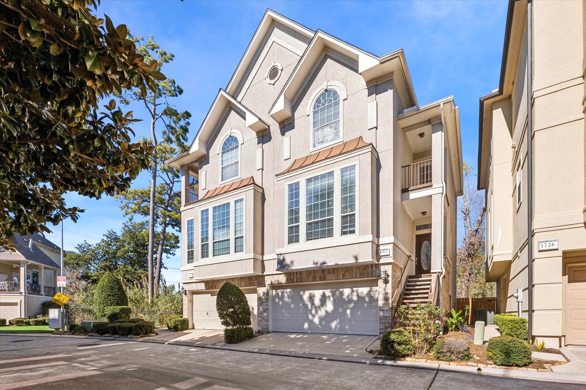 This photo showcases a modern three-story townhouse with a two-car garage and a welcoming entrance. It features large windows, a neat driveway, and well-maintained landscaping, situated in a quiet neighborhood setting.