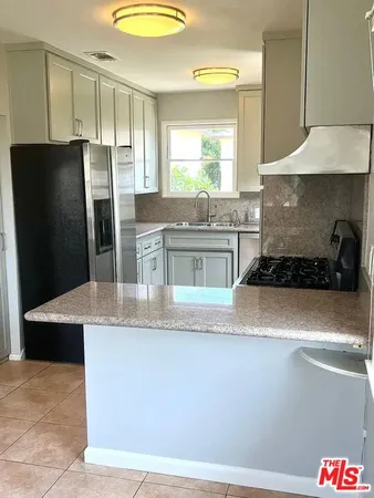 a kitchen with kitchen island granite countertop a refrigerator a sink a stove and wooden cabinets