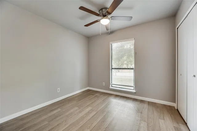 an empty room with wooden floor ceiling fan and windows