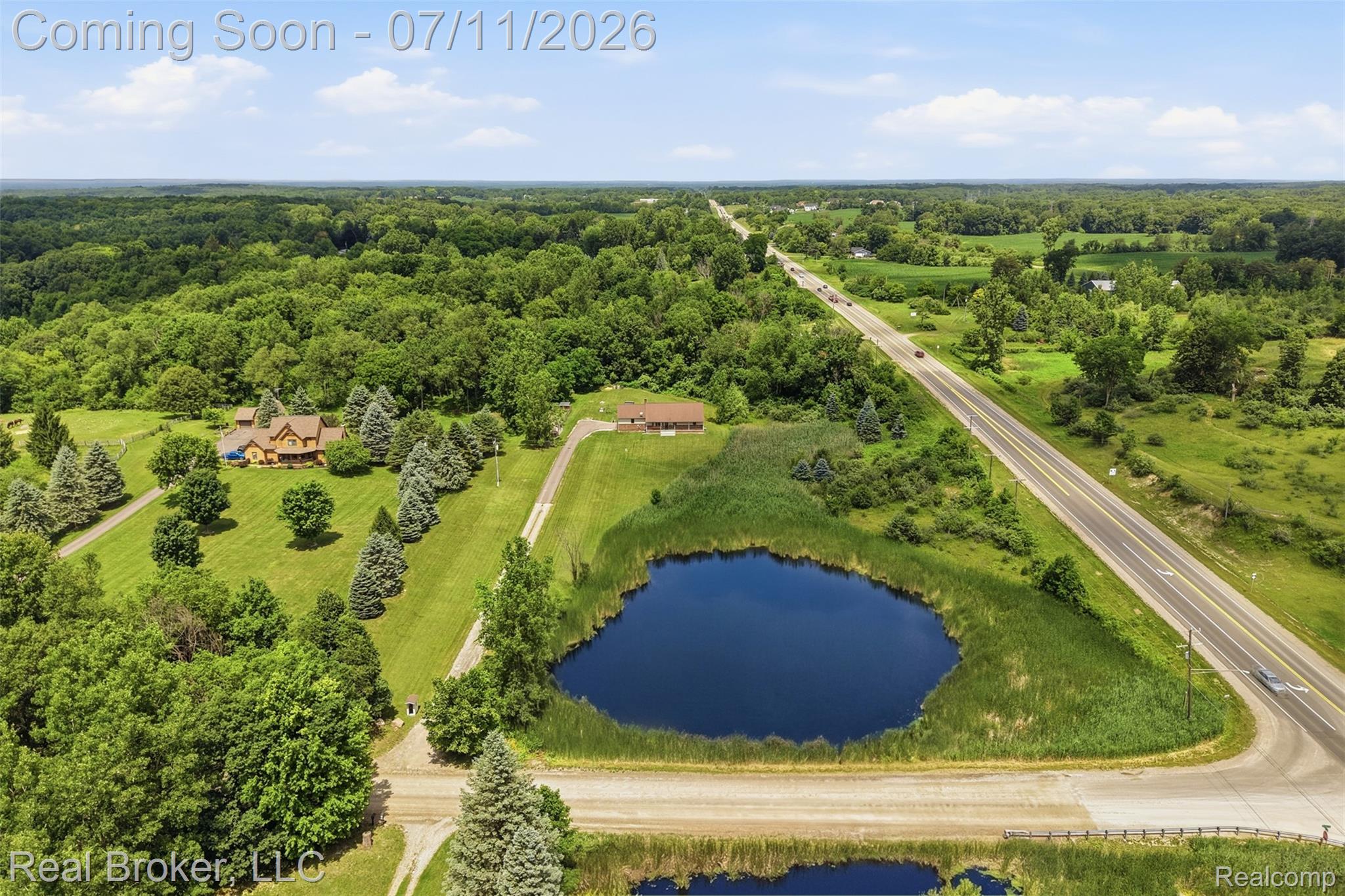 1050 West Brocker Road Metamora, MI 48455 - Photo 49 of 55 Expansive property featuring a prominent pond with surrounding reeds, a paved road, and a gravel driveway
