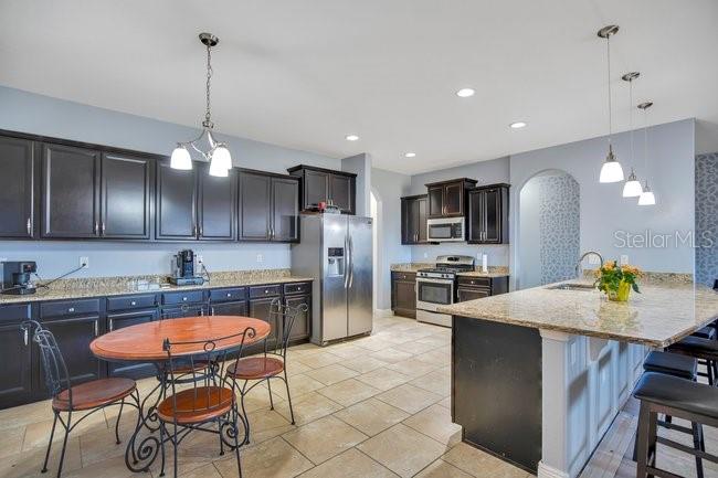 1422 Sharon Rose Trace Deltona, FL 32725 - Photo 8 of 42 a kitchen with stainless steel appliances granite countertop a stove a sink a refrigerator a kitchen island a table and chairs