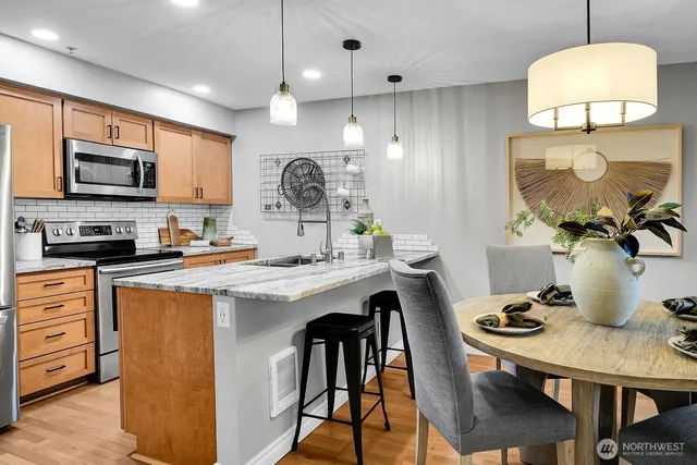 a kitchen with stainless steel appliances granite countertop a kitchen island a stove a sink a dining table and chairs with wooden floor