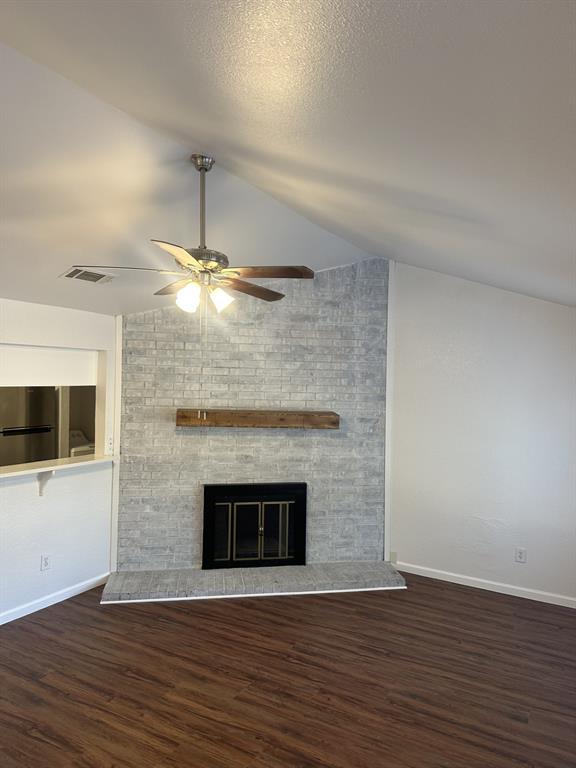 2400 Jupiter Road, Unit D2 Plano, TX 75074 - Photo 1 of 17 Unfurnished living room with a large fireplace, vaulted ceiling, dark wood-style floors, a ceiling fan, and a textured ceiling
