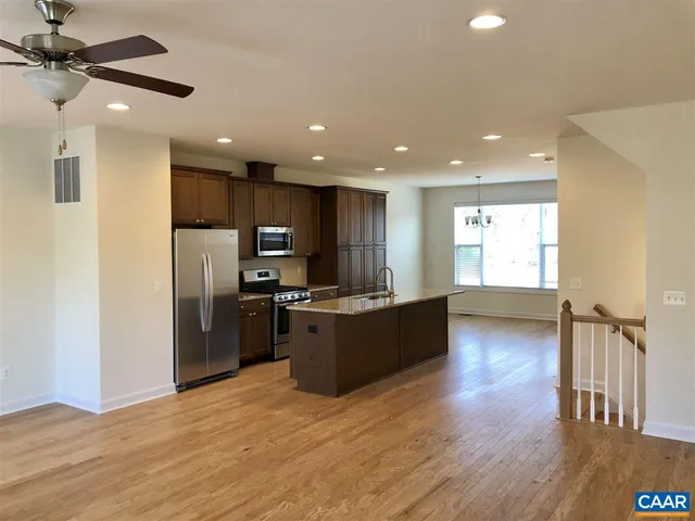 a kitchen with stainless steel appliances kitchen island granite countertop a refrigerator a sink dishwasher a stove and a microwave oven on the wooden floor
