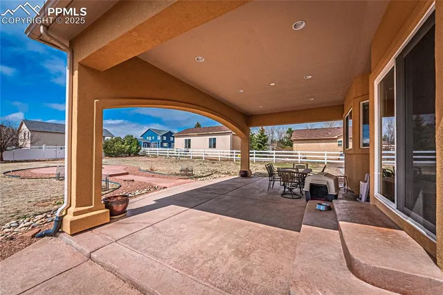 a view of a patio with a table and chairs floor to ceiling window and wooden fence
