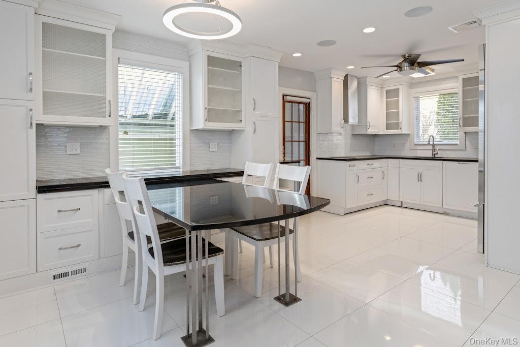 Kitchen with dark countertops, white cabinetry, light tile flooring, glass insert cabinets, and recessed lighting.