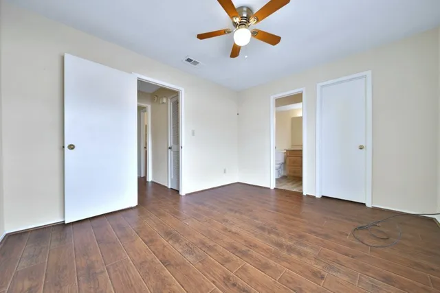 an empty room with wooden floor chandelier fan and windows