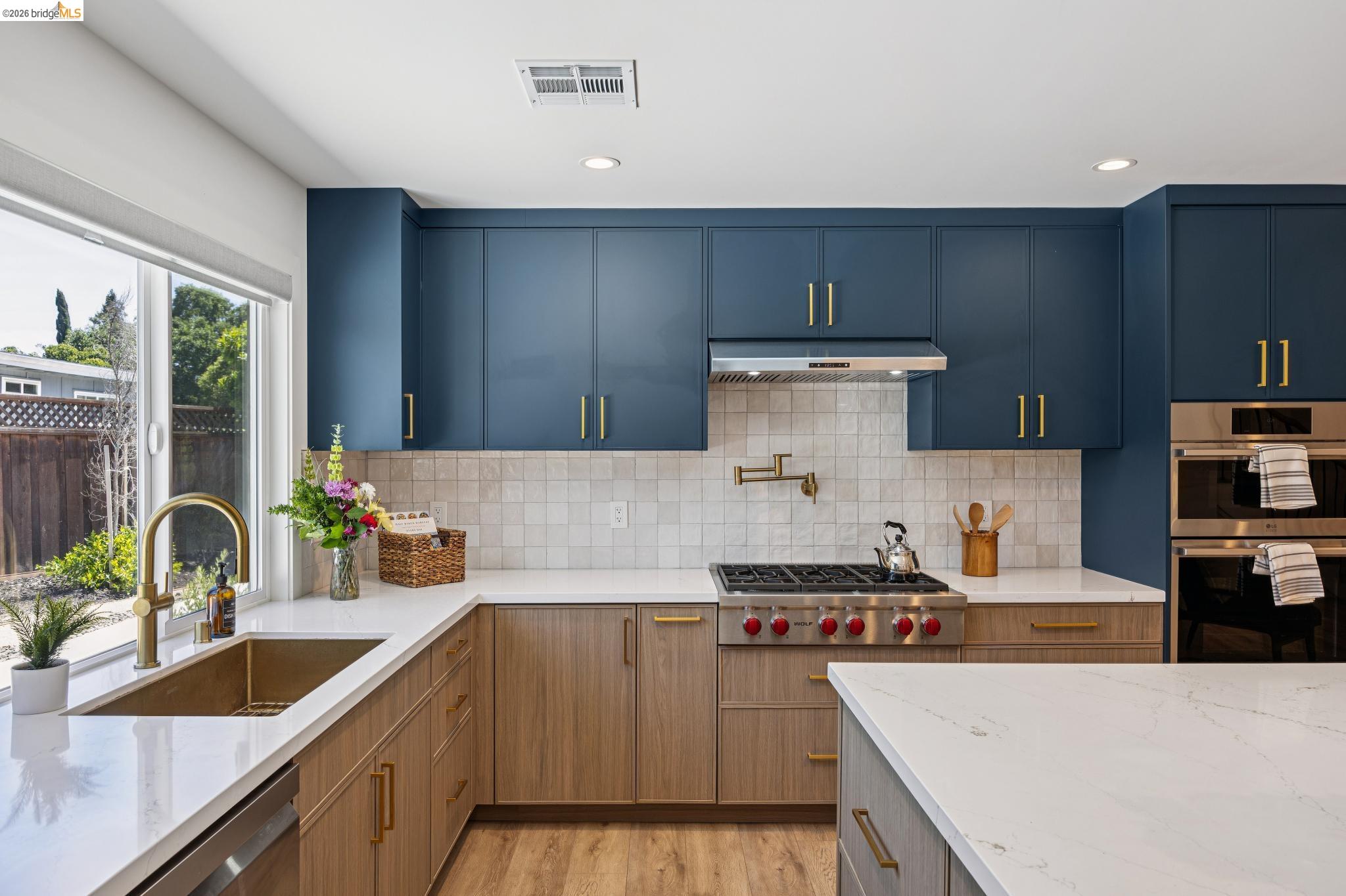 11 Belinda Court San Ramon, CA 94583 - Photo 9 of 33 Modern kitchen featuring two-tone cabinetry with blue upper cabinets and wood-finish lower cabinets, brass hardware, white countertops, and a full-height tiled backsplash