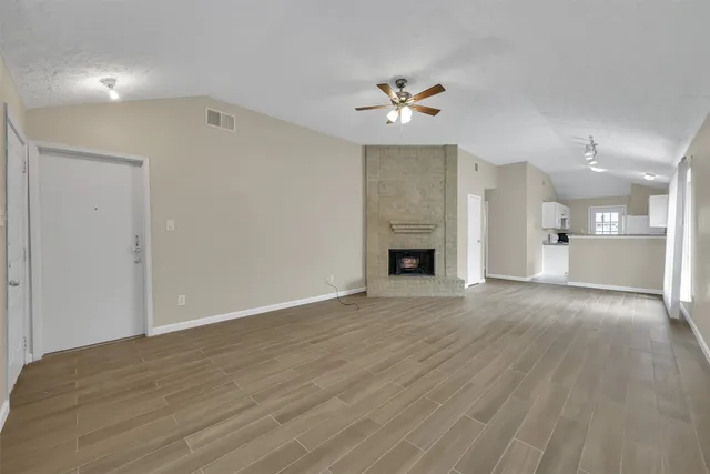 a view of an empty room with wooden floor and a kitchen