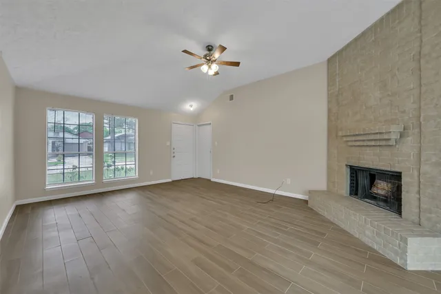 a view of an empty room with wooden floor fireplace and a window