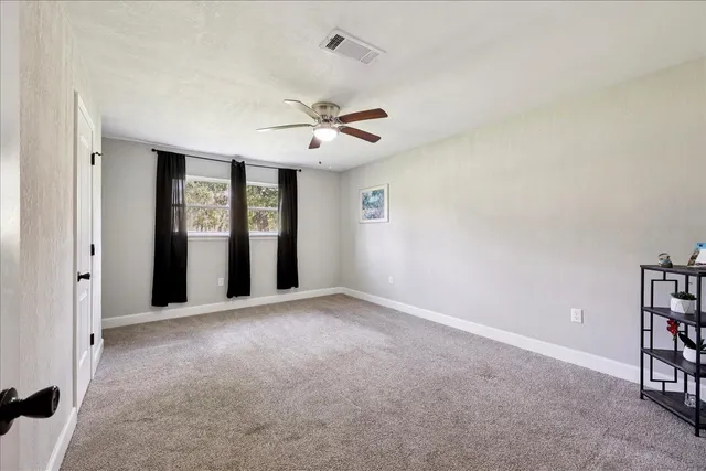 an empty room with chandelier fan and windows