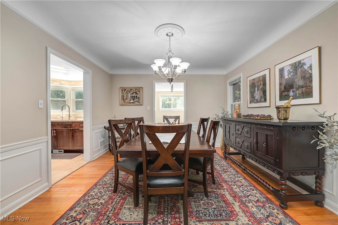 4022 Hillbrook Road Cleveland, OH 44118 - Photo 12 of 49 Dining space featuring wainscoting, light wood finished floors, a chandelier, a decorative wall, and ornamental molding