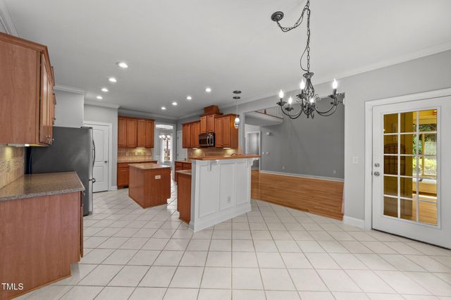 a room with kitchen island granite countertop stainless steel appliances lots of counter top space cabinets and a chandelier
