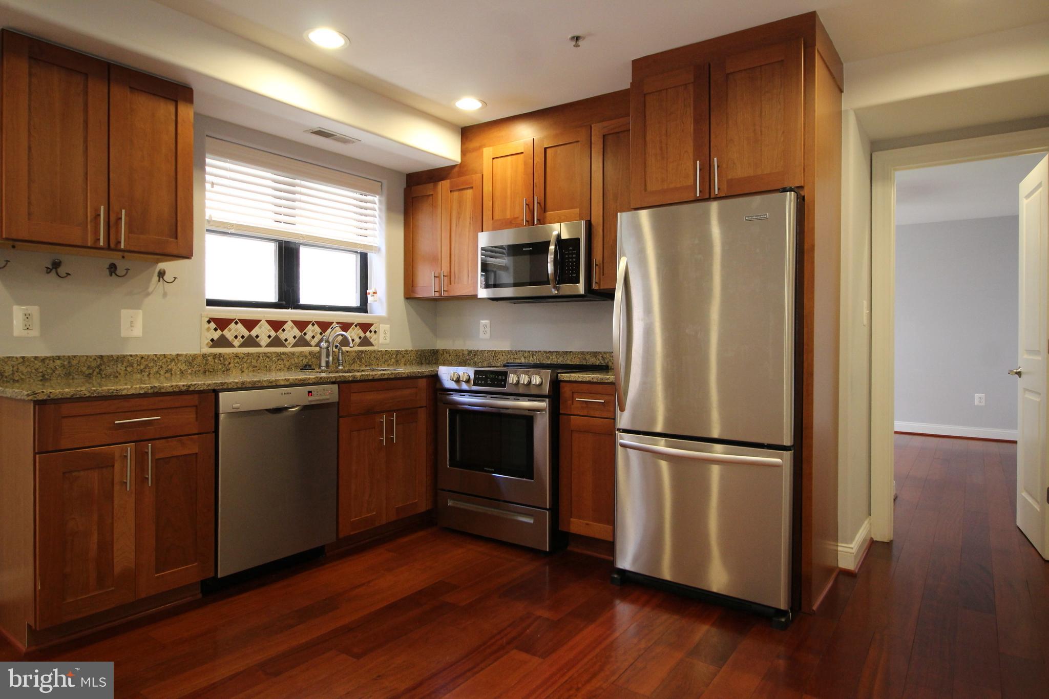 1354 Euclid Street Northwest, Unit 303B Washington, DC 20009 - Photo 8 of 16 a kitchen with granite countertop stainless steel appliances a refrigerator cabinets and wooden floor