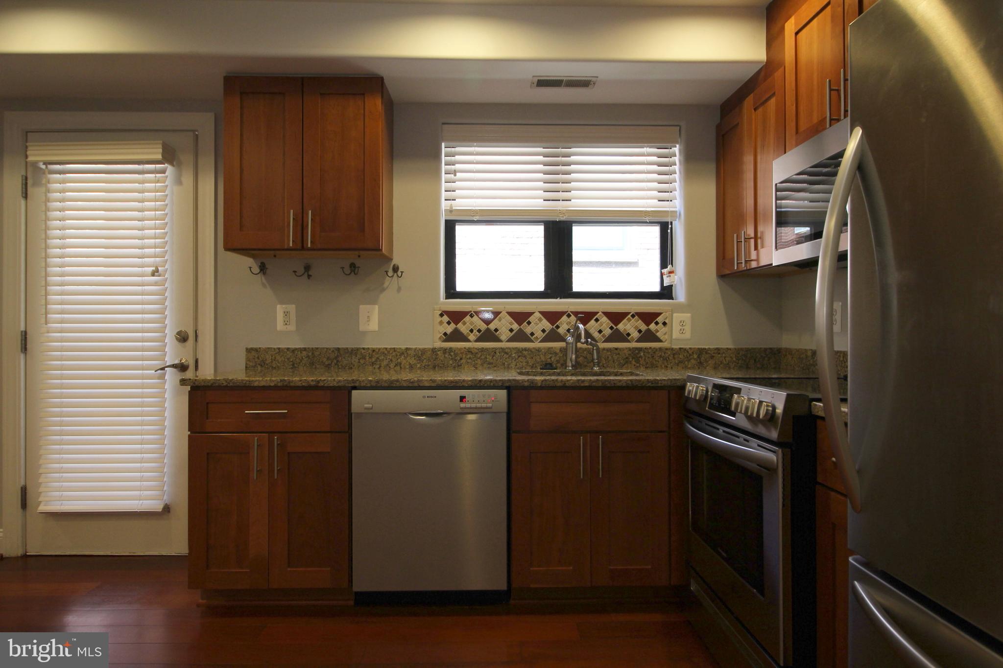 1354 Euclid Street Northwest, Unit 303B Washington, DC 20009 - Photo 10 of 16 a kitchen with granite countertop cabinets stainless steel appliances a window and wooden floor