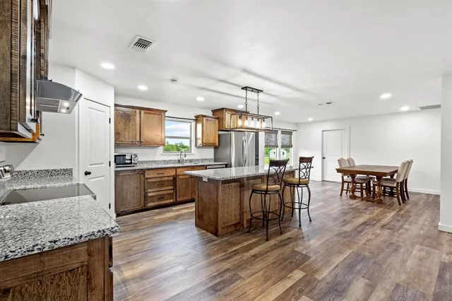 a kitchen with stainless steel appliances granite countertop a table chairs sink and cabinets