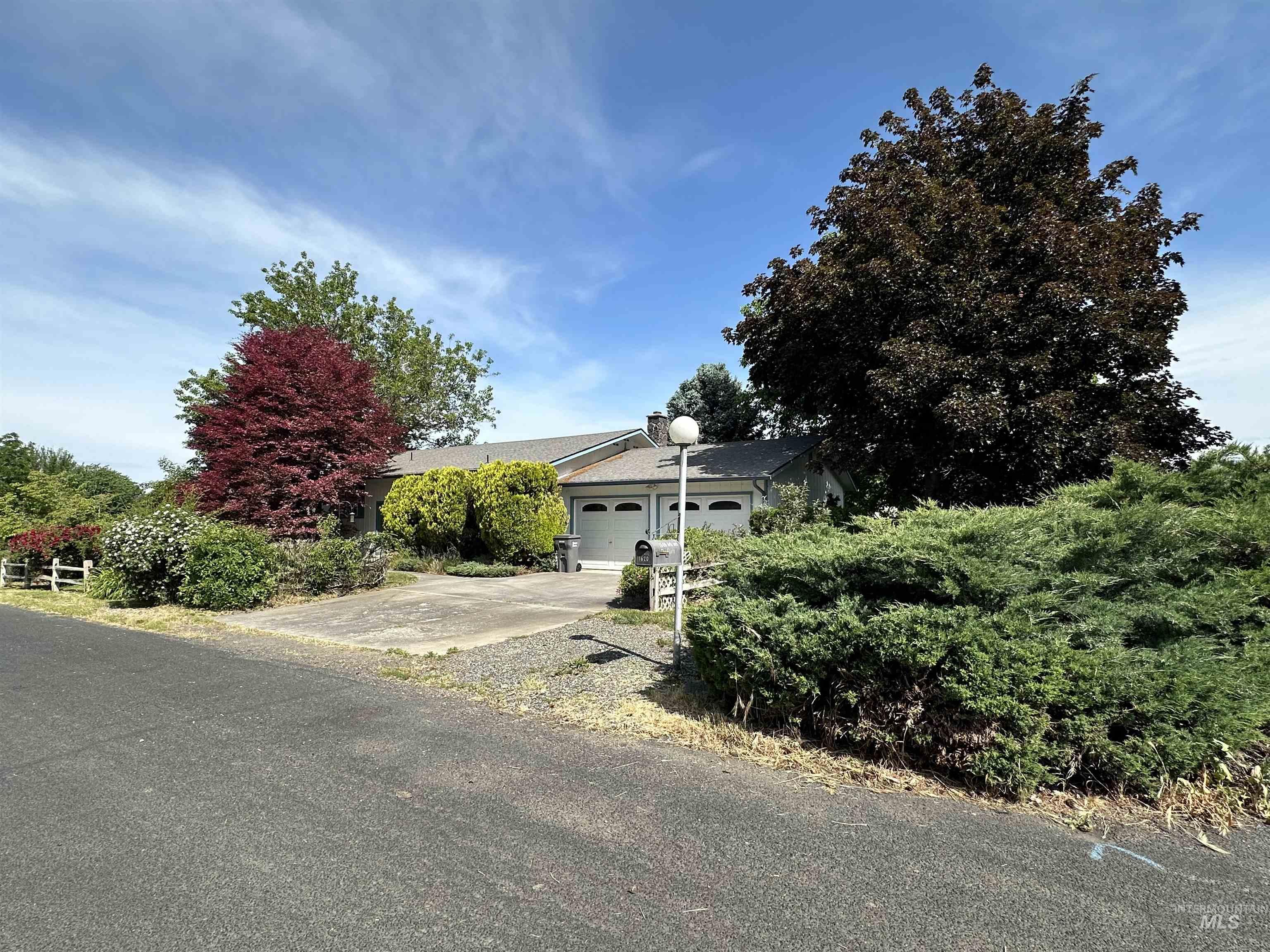 1620 6th Avenue Clarkston, WA 99403 - Photo 2 of 19 Ranch-style residence featuring a two-car garage with white doors, mature trees, diverse plantings, and a paved driveway