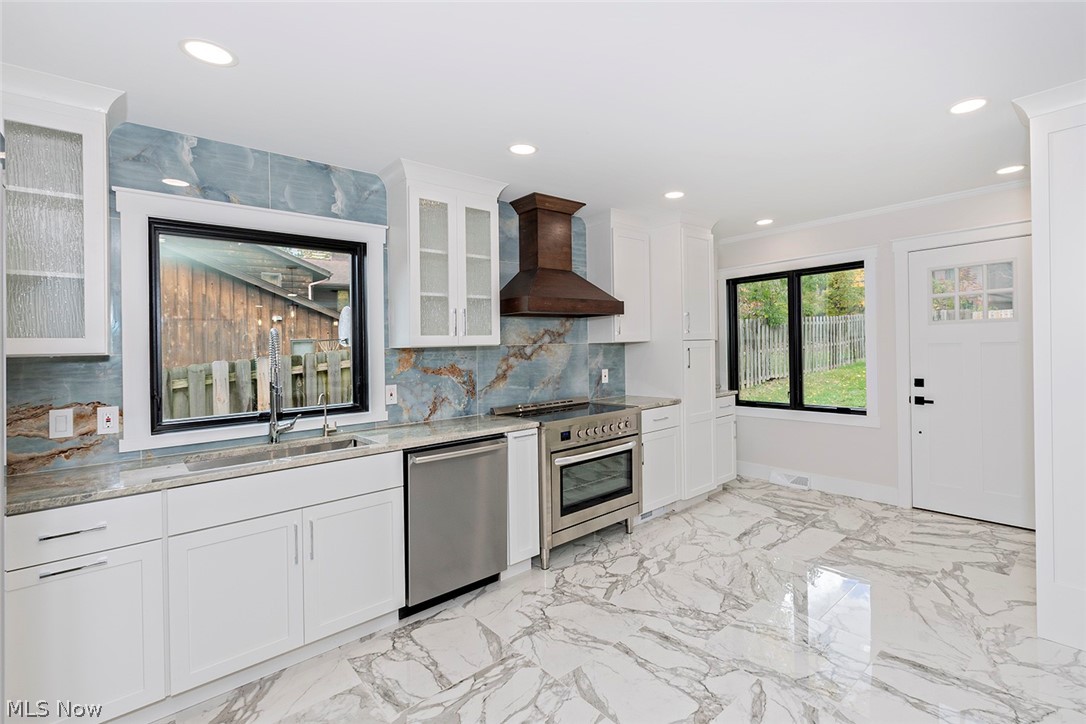 20601 Shelburne Road Shaker Heights, OH 44122 - Photo 10 of 29 Kitchen with wall chimney exhaust hood, white cabinetry, light marble finish flooring, appliances with stainless steel finishes, and light stone counters
