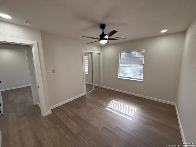 an empty room with wooden floor ceiling fan and windows