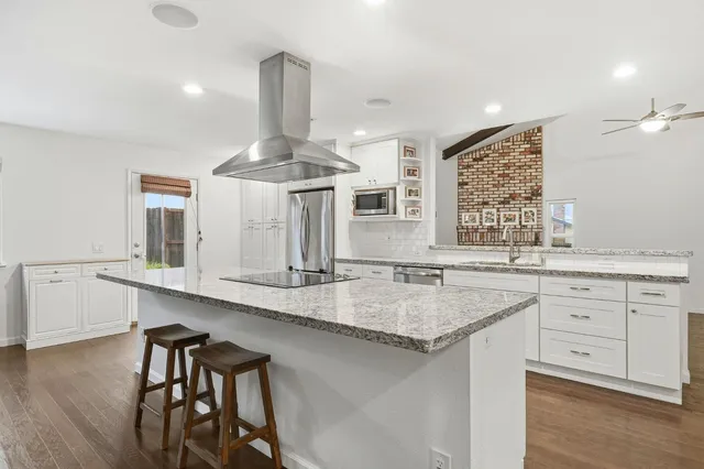 a kitchen with stainless steel appliances a refrigerator a sink dishwasher a stove and white cabinets with wooden floor