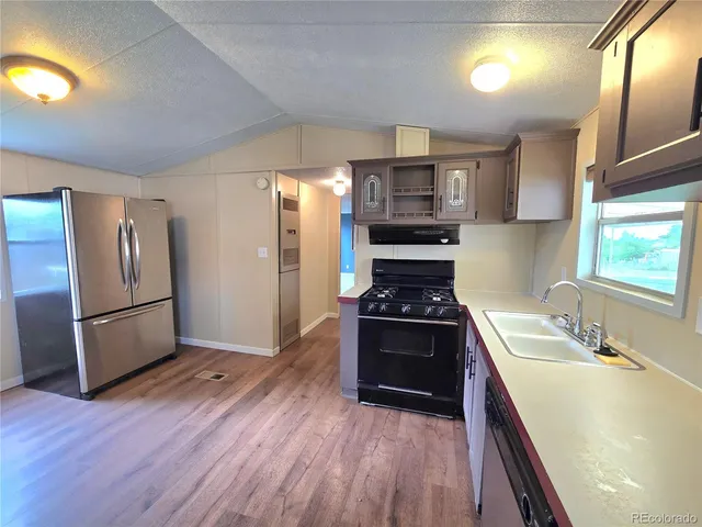 a kitchen with stainless steel appliances a refrigerator a sink a stove a microwave a sink a refrigerator wooden floor and cabinets