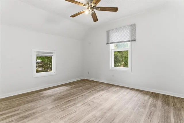 an empty room with wooden floor window and ceiling fan