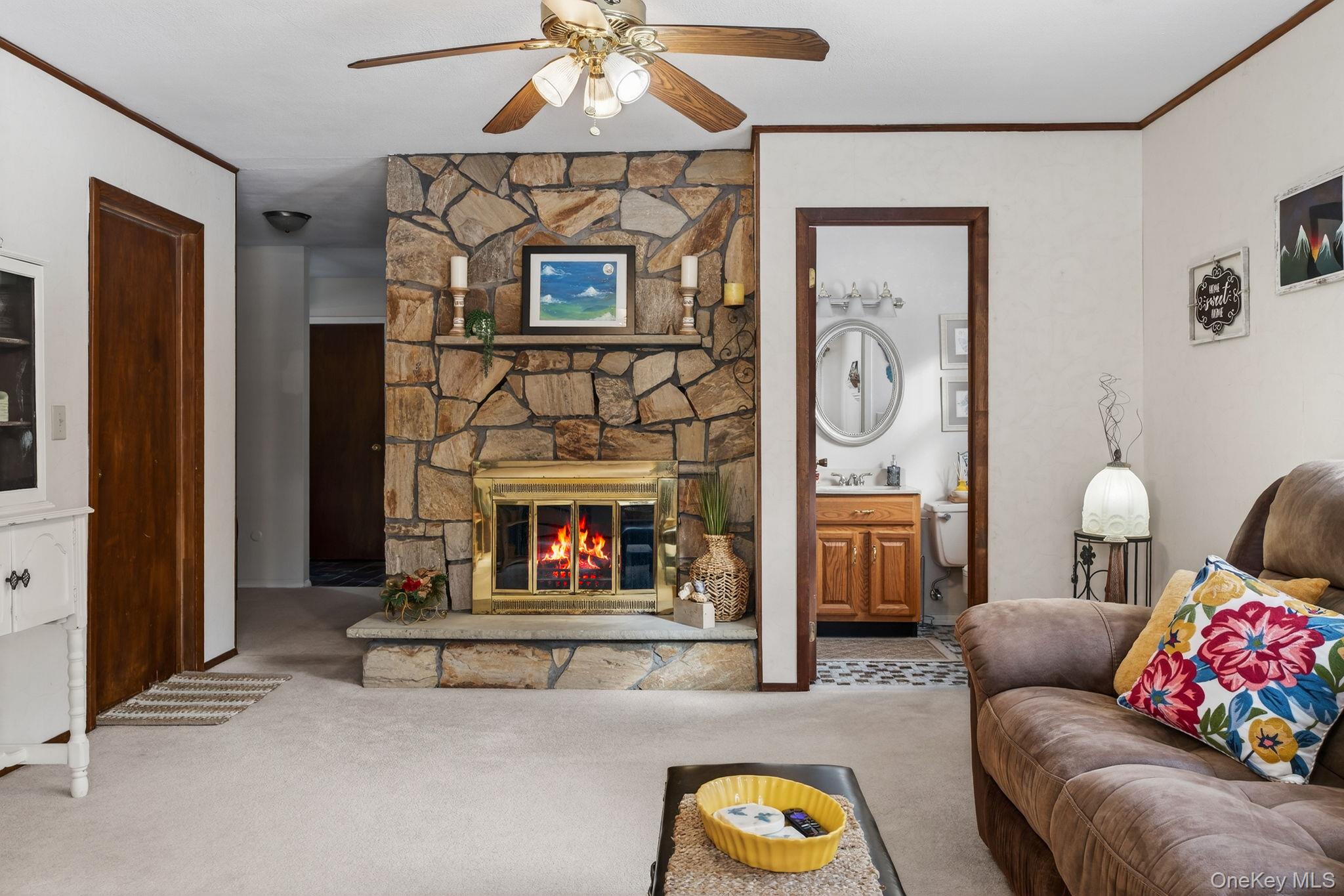 15 Royal Oak Road Stone Ridge, NY 12484 - Photo 28 of 34 Living area featuring ornamental molding, a stone fireplace, carpet flooring, and a ceiling fan