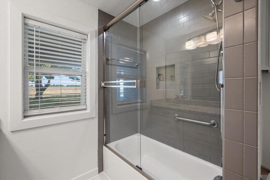 917 Goodwyn Road Italy, TX 76651 - Photo 23 of 40 Tub/shower combination featuring a glass sliding door, subway tile surround, and a built-in niche