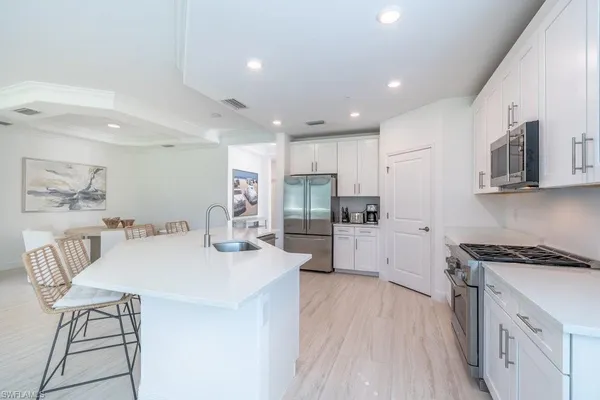 a kitchen with stainless steel appliances kitchen island granite countertop a stove a sink a refrigerator and white cabinets with wooden floor