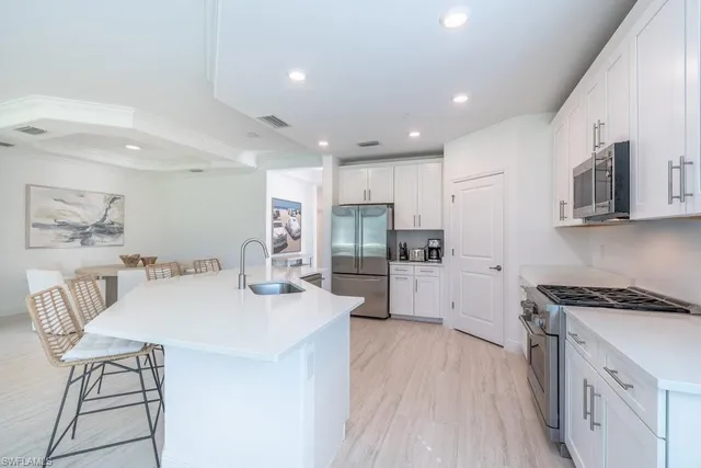 a kitchen with stainless steel appliances kitchen island granite countertop a stove a sink a refrigerator and white cabinets with wooden floor