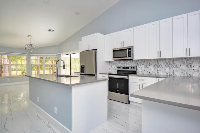 a kitchen with stainless steel appliances granite countertop a refrigerator stove a sink and white cabinets