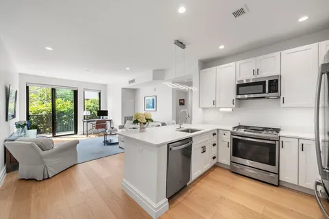 a open kitchen with stainless steel appliances granite countertop a stove top oven a sink dishwasher a dining table and chairs with wooden floor
