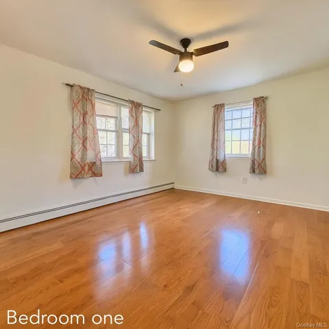 an empty room with wooden floor fan and windows