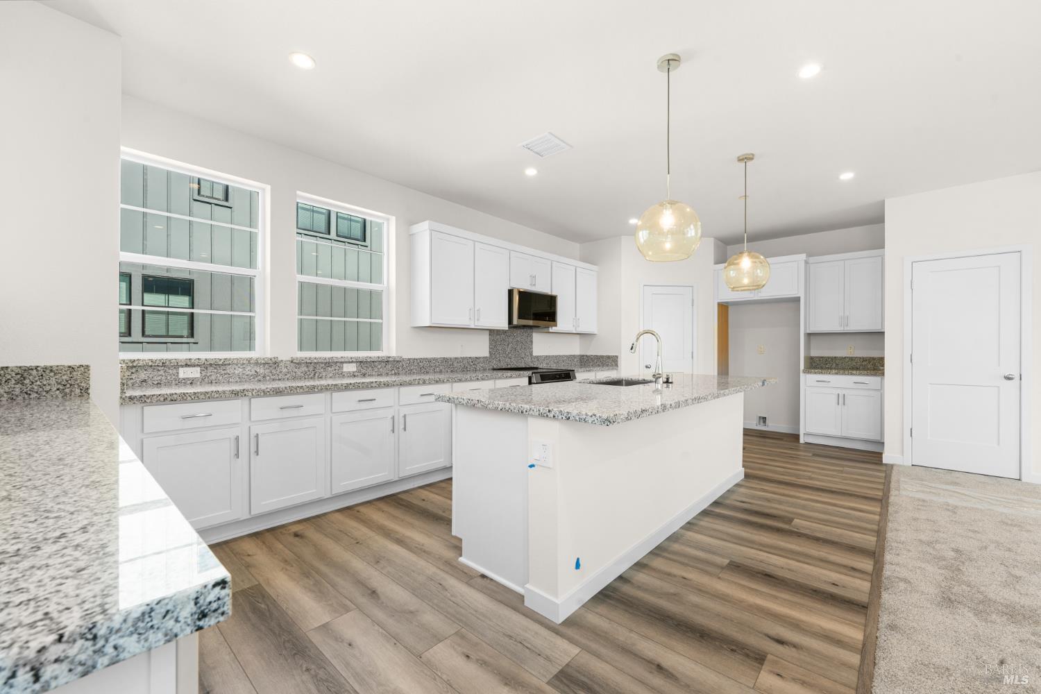 a large kitchen with granite countertop a stove a sink a refrigerator and white cabinets with wooden floor