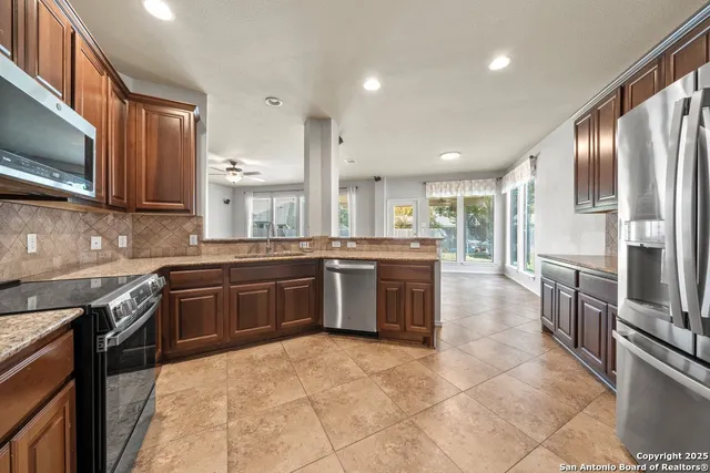 a large kitchen with stainless steel appliances granite countertop a stove top oven a sink and a refrigerator