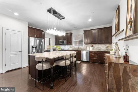 a dining hall with stainless steel appliances kitchen island granite countertop a refrigerator a stove a sink dishwasher a dining table and chairs with wooden floor
