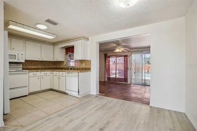 a large white kitchen with granite countertop a stove top oven a sink and white cabinets with wooden floor