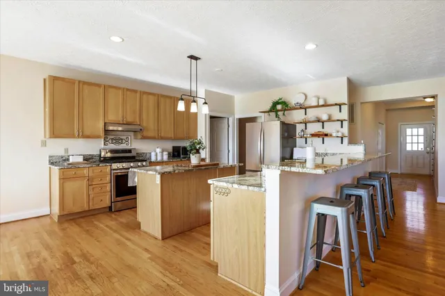 a large kitchen with stainless steel appliances granite countertop a stove top oven a sink dishwasher a dining table and chairs with wooden floor