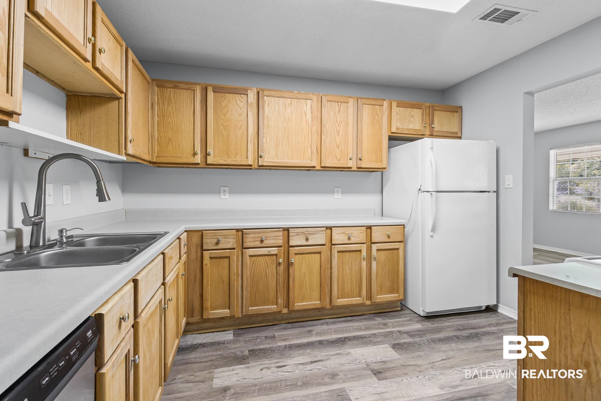 6933 Burbank Court Mobile, AL 36619 - Photo 12 of 25 Kitchen featuring wood cabinetry, light countertops, wood-finish flooring, a stainless steel double basin sink with a gooseneck faucet, and a skylight