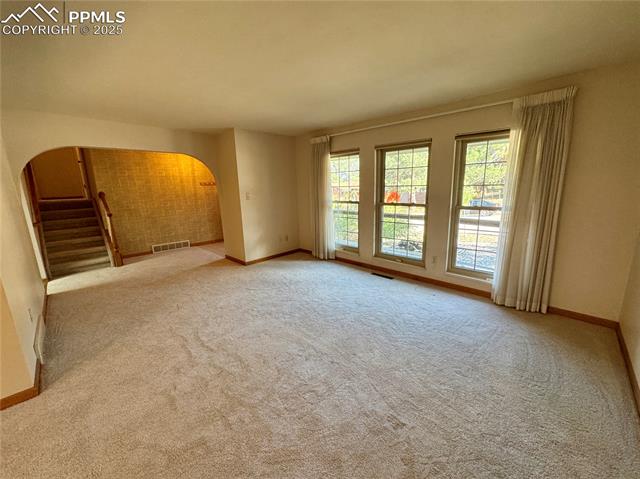 280 Raven Hills Road Colorado Springs, CO 80919 - Photo 16 of 48 Empty room with visible vents, arched walkways, baseboards, and carpet floors