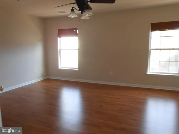 an empty room with wooden floor chandelier fan and windows