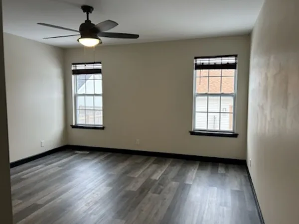 an empty room with wooden floor chandelier fan and windows