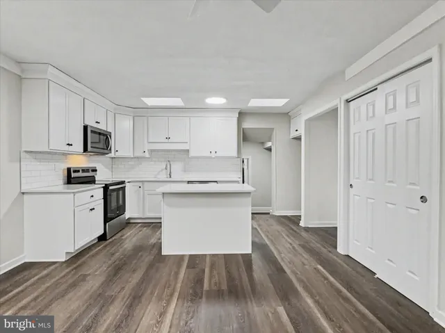 a kitchen with stainless steel appliances a stove top oven a sink a refrigerator white cabinets and wooden floor