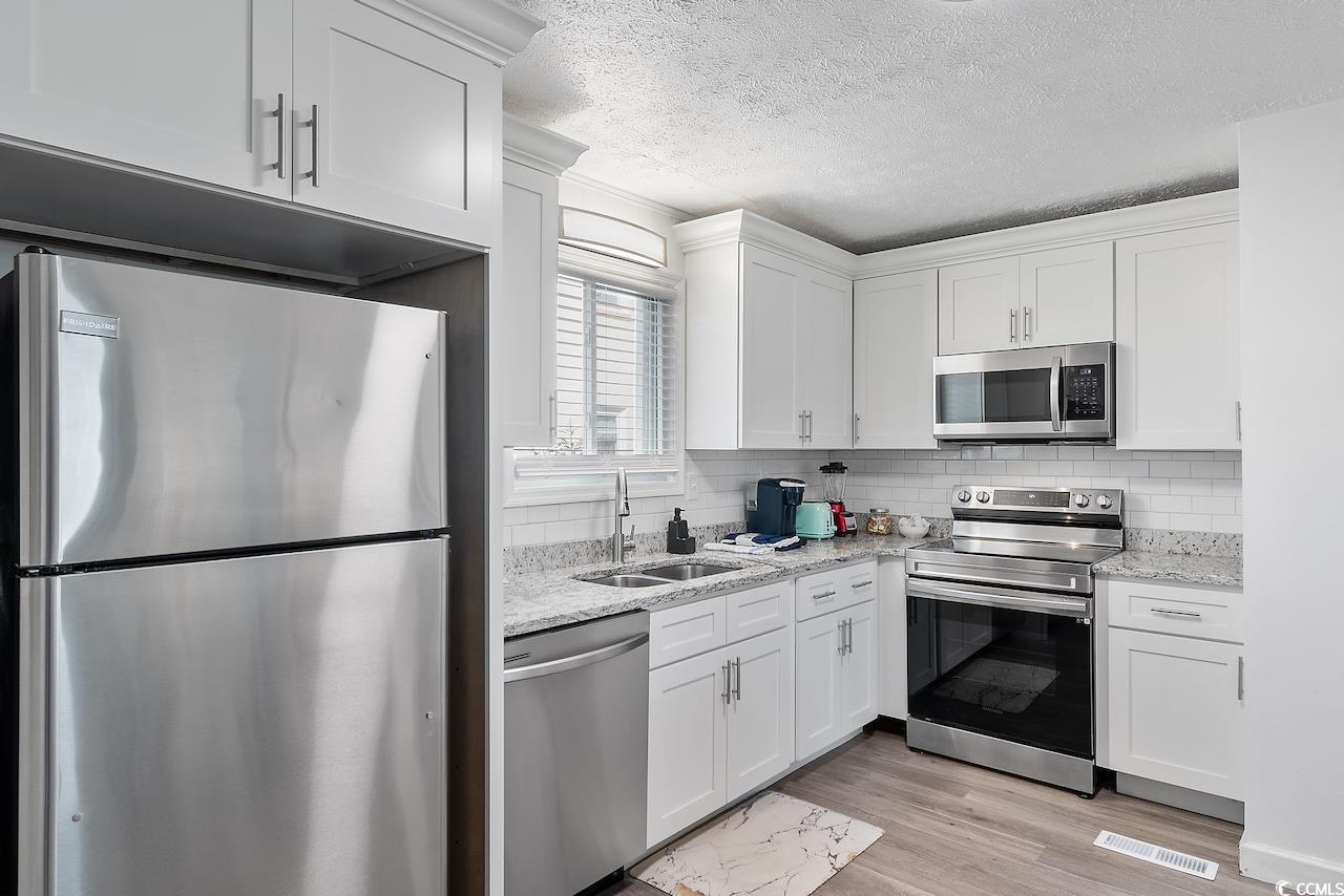 409 17th Avenue North, Unit 4 Myrtle Beach, SC 29577 - Photo 11 of 22 Kitchen with stainless steel appliances, a textured ceiling, light stone countertops, white cabinetry, and light wood-style flooring