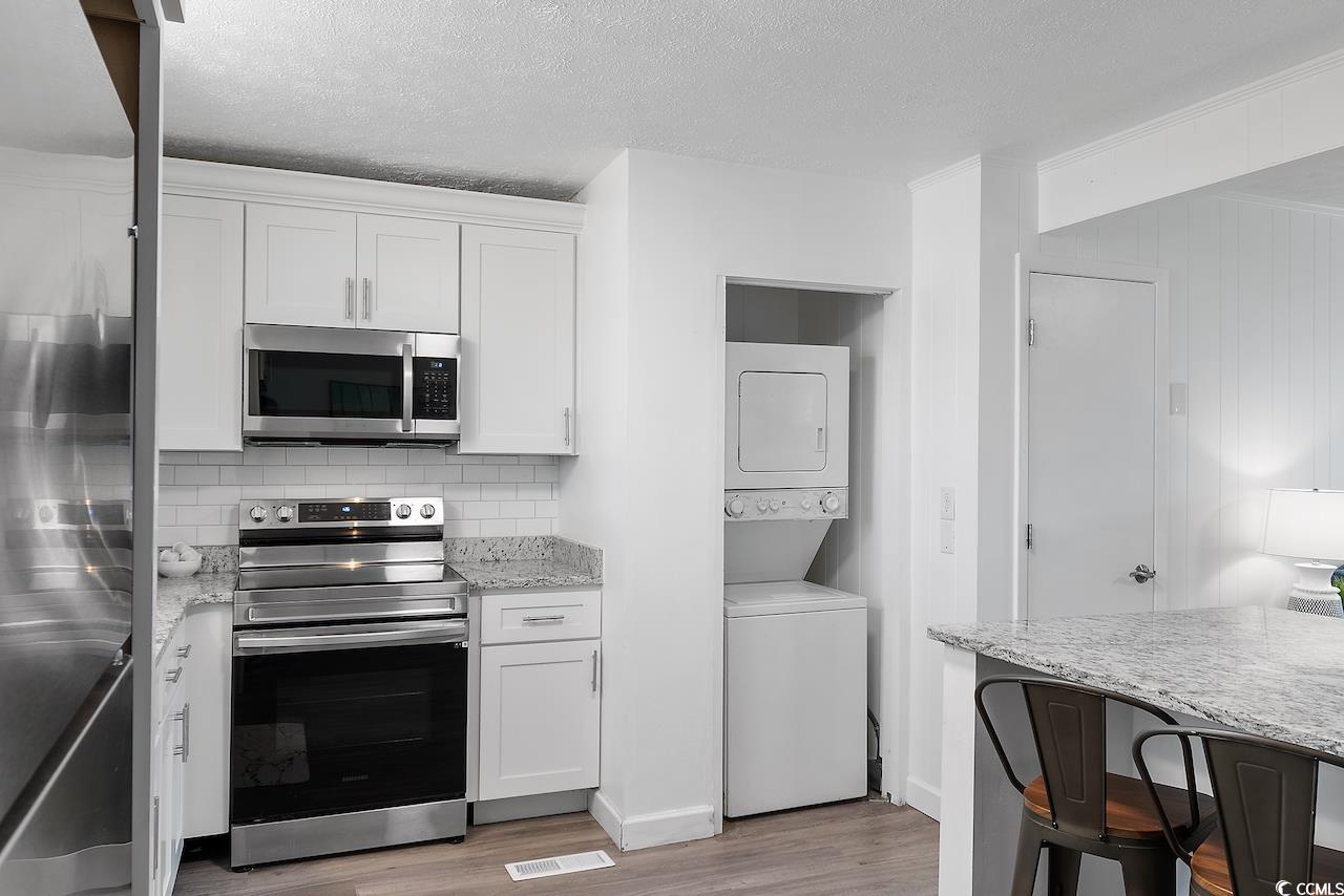 409 17th Avenue North, Unit 4 Myrtle Beach, SC 29577 - Photo 12 of 22 Kitchen featuring stainless steel appliances, stacked washer / dryer, light wood-type flooring, white cabinetry, and a textured ceiling
