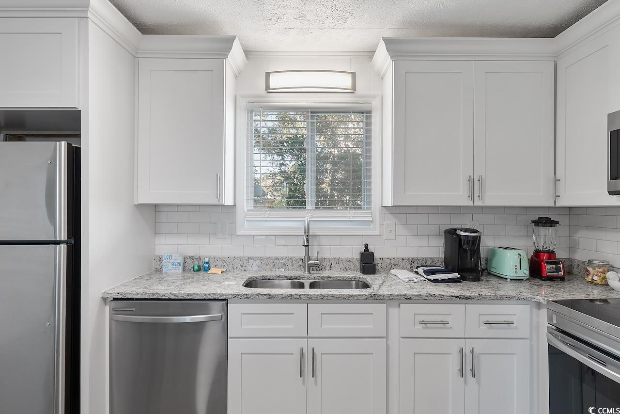 409 17th Avenue North, Unit 4 Myrtle Beach, SC 29577 - Photo 13 of 22 Kitchen with stainless steel appliances, tasteful backsplash, light stone counters, white cabinets, and a textured ceiling