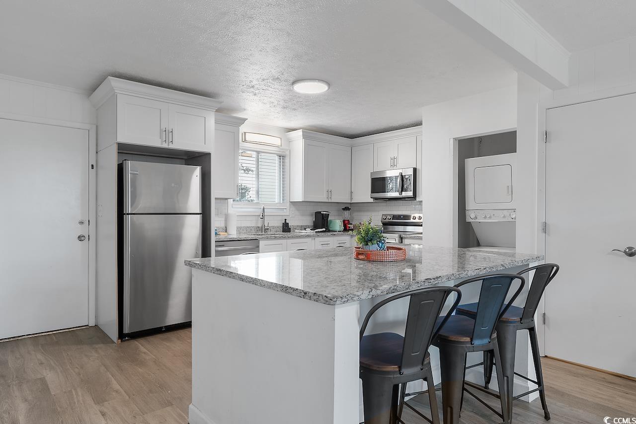 409 17th Avenue North, Unit 4 Myrtle Beach, SC 29577 - Photo 7 of 22 Kitchen featuring stainless steel appliances, light stone countertops, a breakfast bar, white cabinetry, and light wood-style flooring