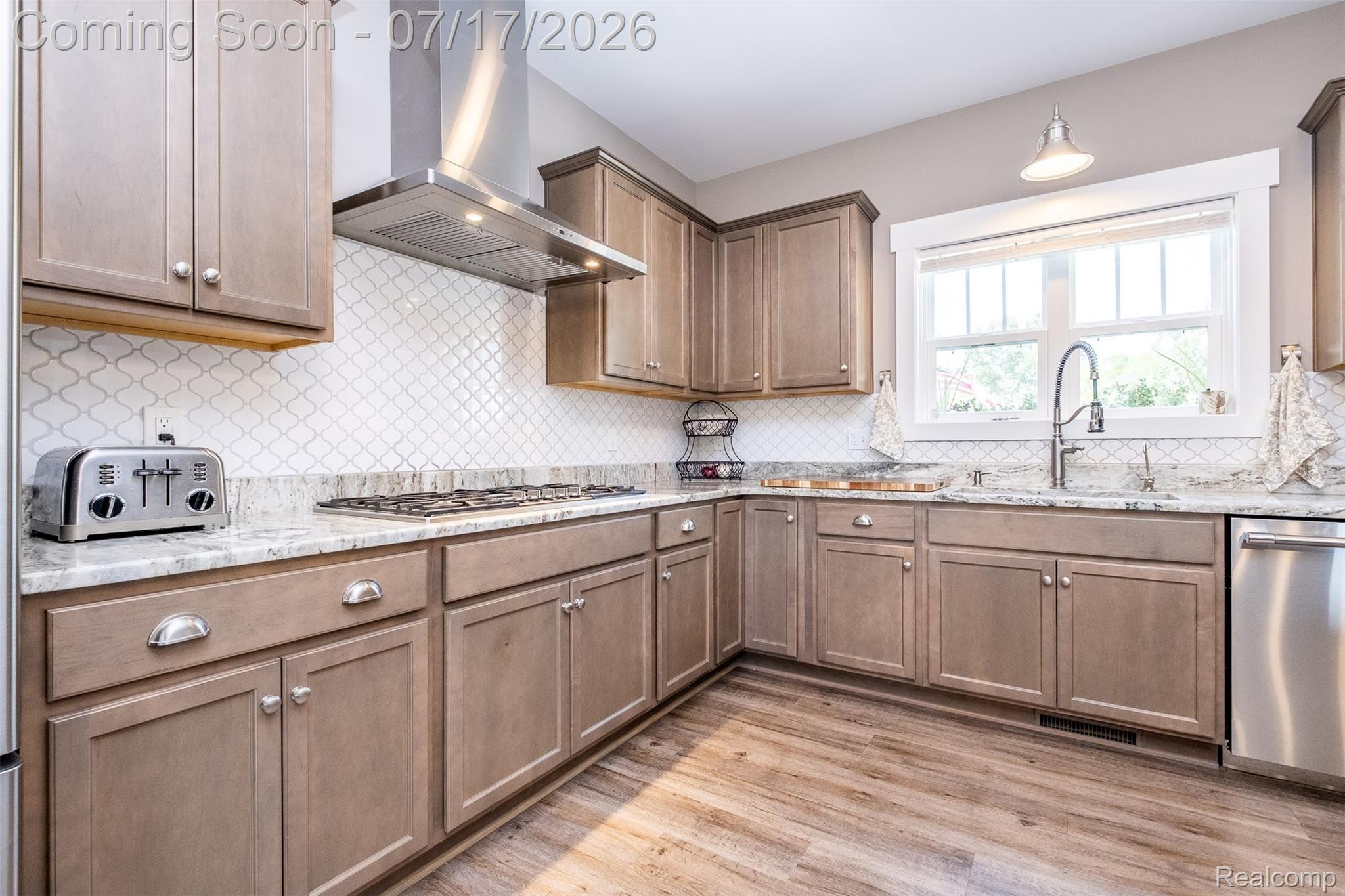 12349 Sugar Maple Drive Fenton, MI 48430 - Photo 15 of 67 Kitchen featuring light-toned cabinetry, light-toned countertops, a white arabesque tile backsplash, stainless steel appliances, and wood-finish flooring
