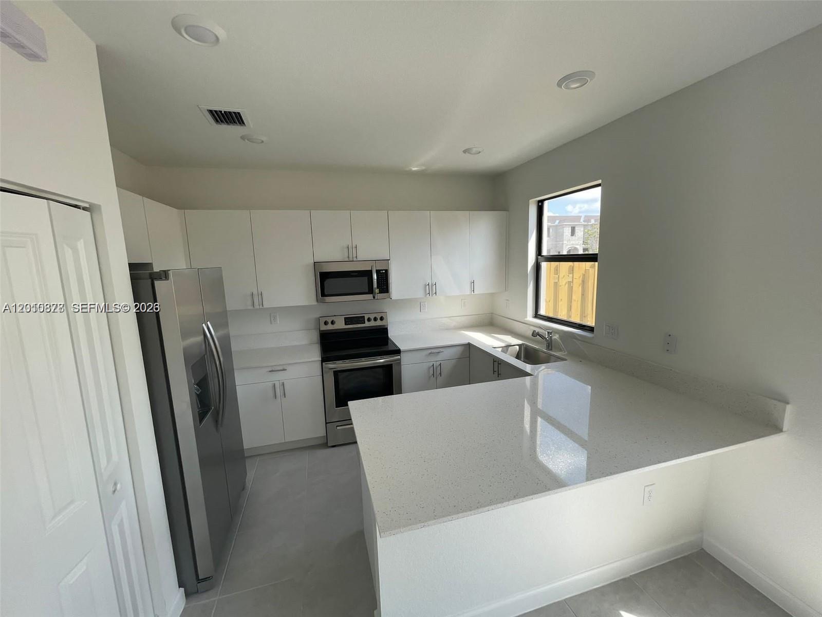24641 Southwest 117th Path, Unit 24641 Homestead, FL 33032 - Photo 4 of 9 a living room with stainless steel appliances a refrigerator a sink a stove a microwave and cabinets