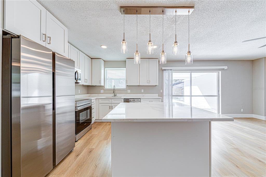 1648 Caldwell Road Daytona Beach, FL 32119 - Photo 18 of 45 a large kitchen with stainless steel appliances kitchen island granite countertop a refrigerator a sink dishwasher a stove and white countertops with wooden floor